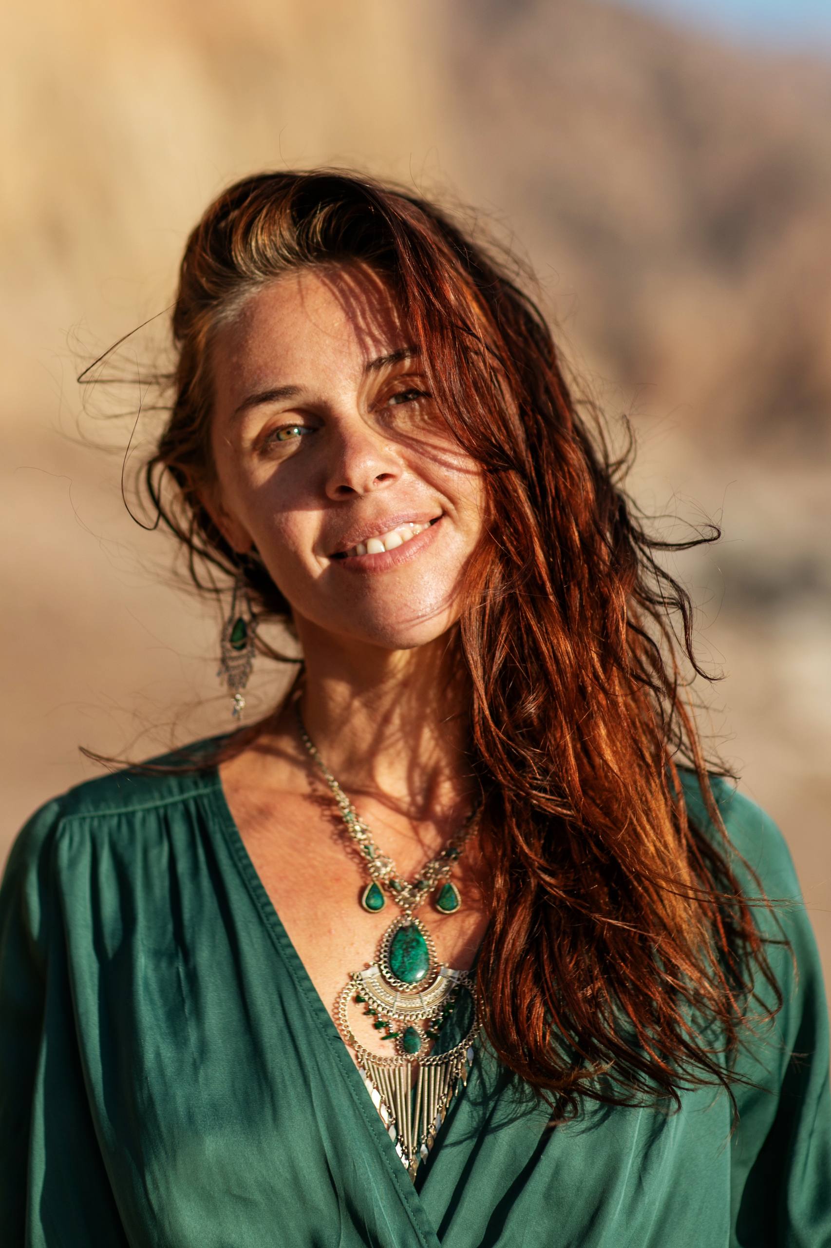 Ela close-up portrait with flowing auburn hair and emerald necklace in golden desert light